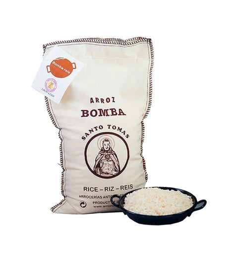 Santo Tomás Arroz Bomba 1 kg – Stoffsack mit Bomba-Paellareis neben einer Paella-Pfanne mit Reis